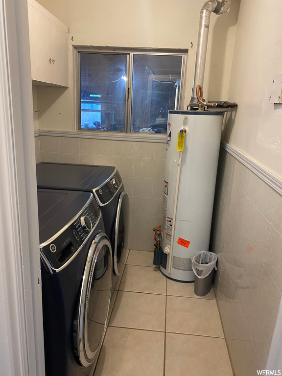 Laundry area with light tile floors, washer and clothes dryer, gas water heater, cabinets, and tile walls