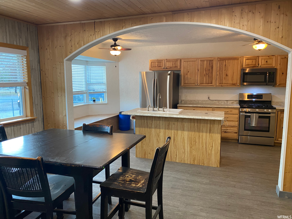 Kitchen featuring wooden walls, appliances with stainless steel finishes, ceiling fan, wood ceiling, and light wood-type flooring