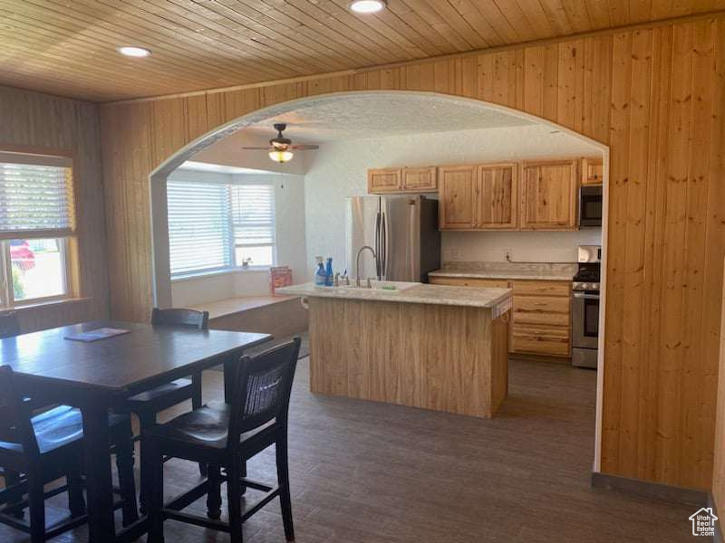 Kitchen featuring a center island with sink, stainless steel appliances, wooden walls, hardwood / wood-style floors, and wood ceiling