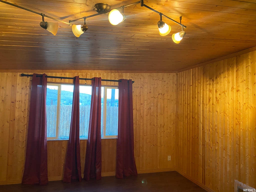 Empty room featuring track lighting, wood ceiling, and wood walls