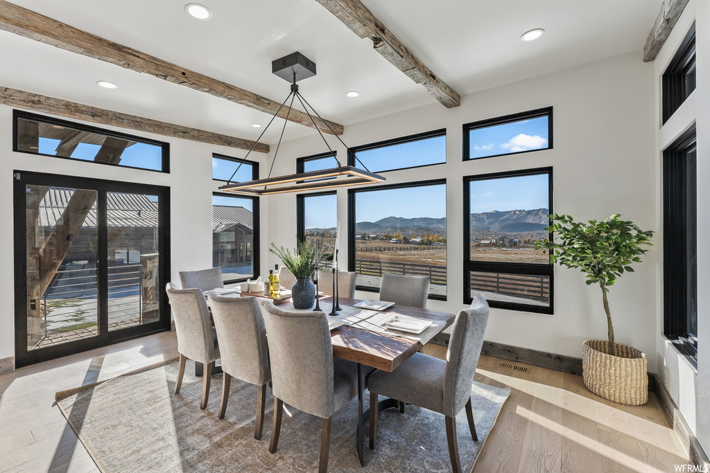 Dining area with light hardwood / wood-style floors, beam ceiling, a mountain view, and a notable chandelier