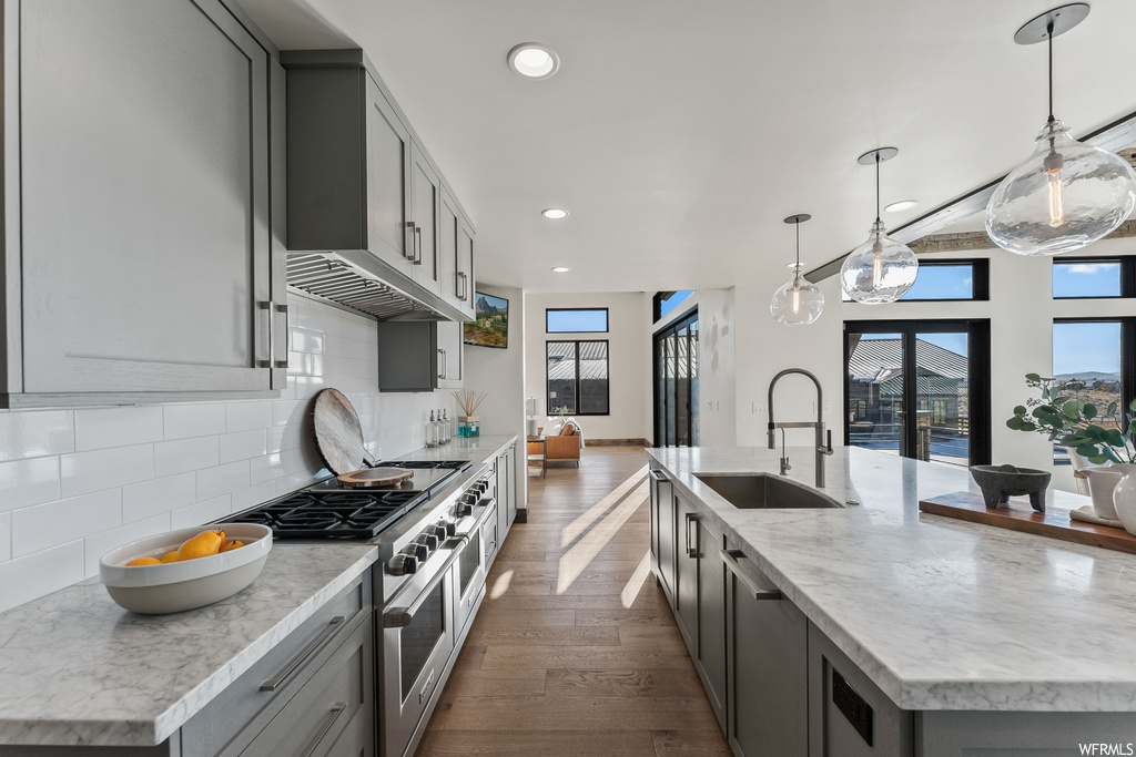 Kitchen featuring double oven range, an island with sink, backsplash, pendant lighting, and dark hardwood / wood-style flooring