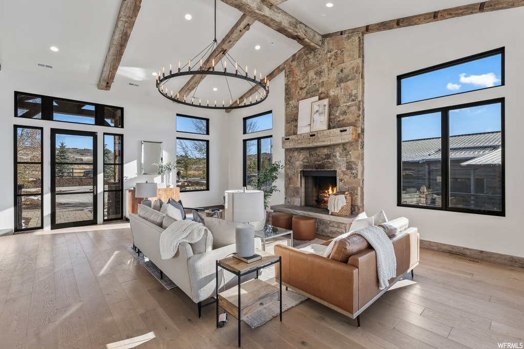 Living room with a stone fireplace, light hardwood / wood-style floors, beamed ceiling, high vaulted ceiling, and a chandelier