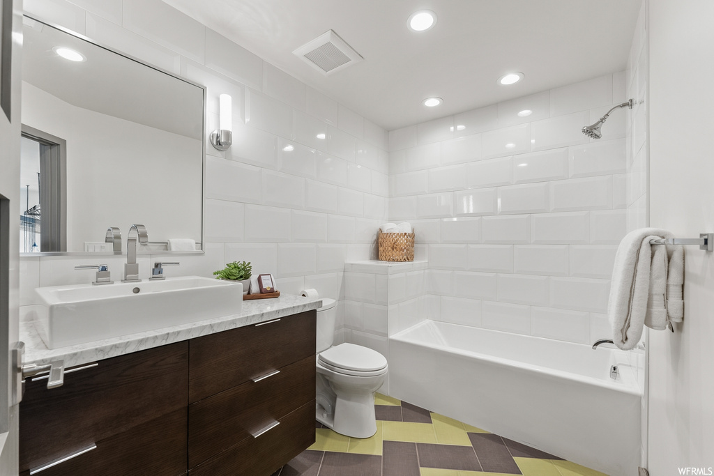 Full bathroom with tiled shower / bath combo, large vanity, toilet, and tile floors
