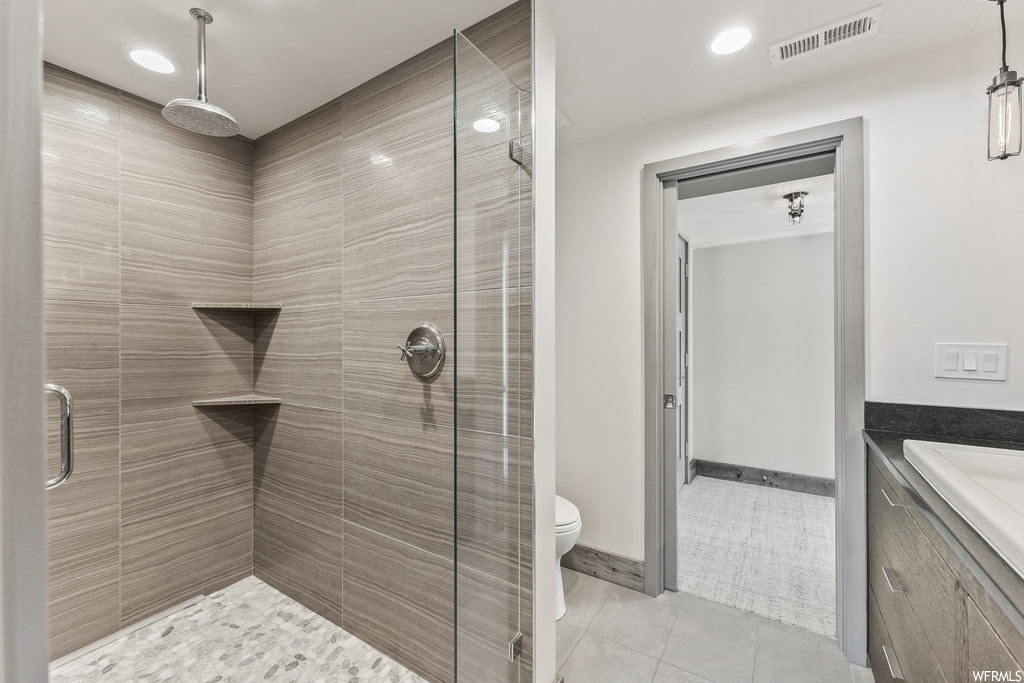 Bathroom featuring tile flooring, vanity, tiled shower, and toilet