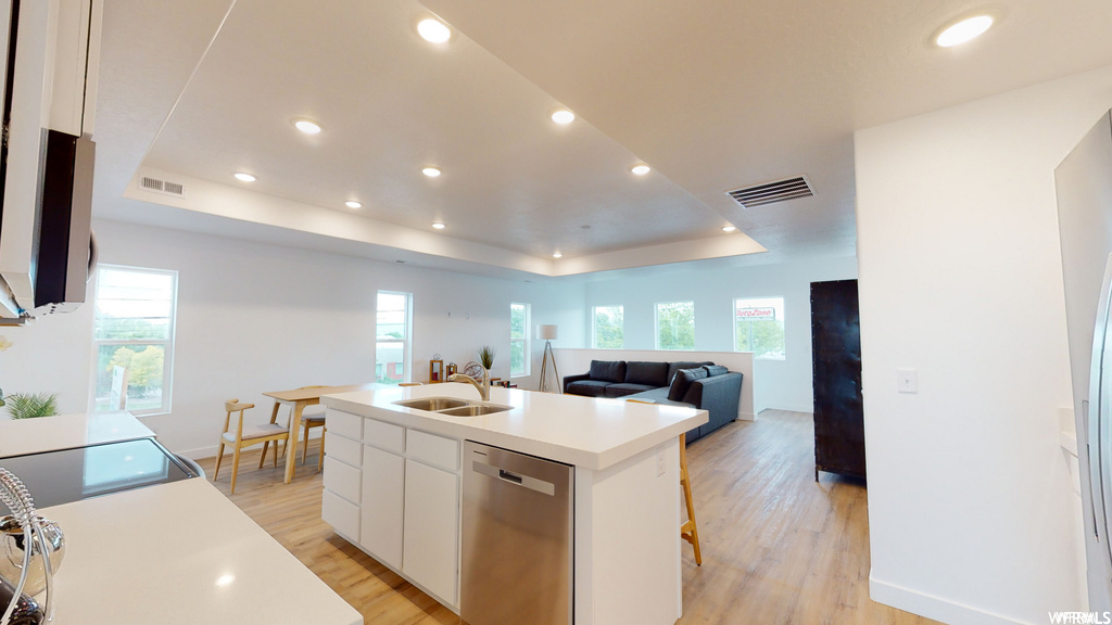 Kitchen featuring sink, light hardwood / wood-style floors, white cabinets, stainless steel dishwasher, and a raised ceiling