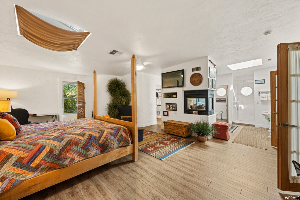 Bedroom featuring a multi sided fireplace, ensuite bathroom, and light hardwood / wood-style flooring
