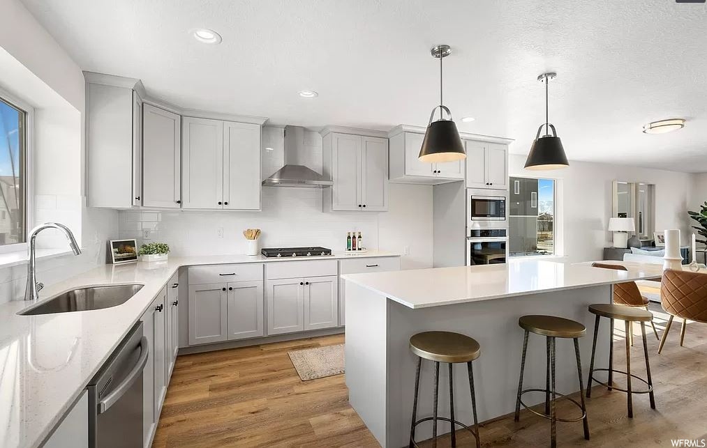 Kitchen featuring a breakfast bar area, light hardwood / wood-style floors, decorative light fixtures, sink, and wall chimney range hood