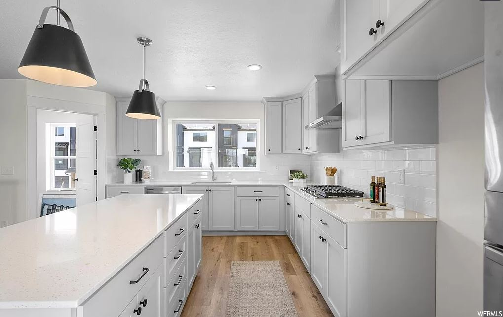 Kitchen with tasteful backsplash, a center island, light wood-type flooring, pendant lighting, and white cabinetry