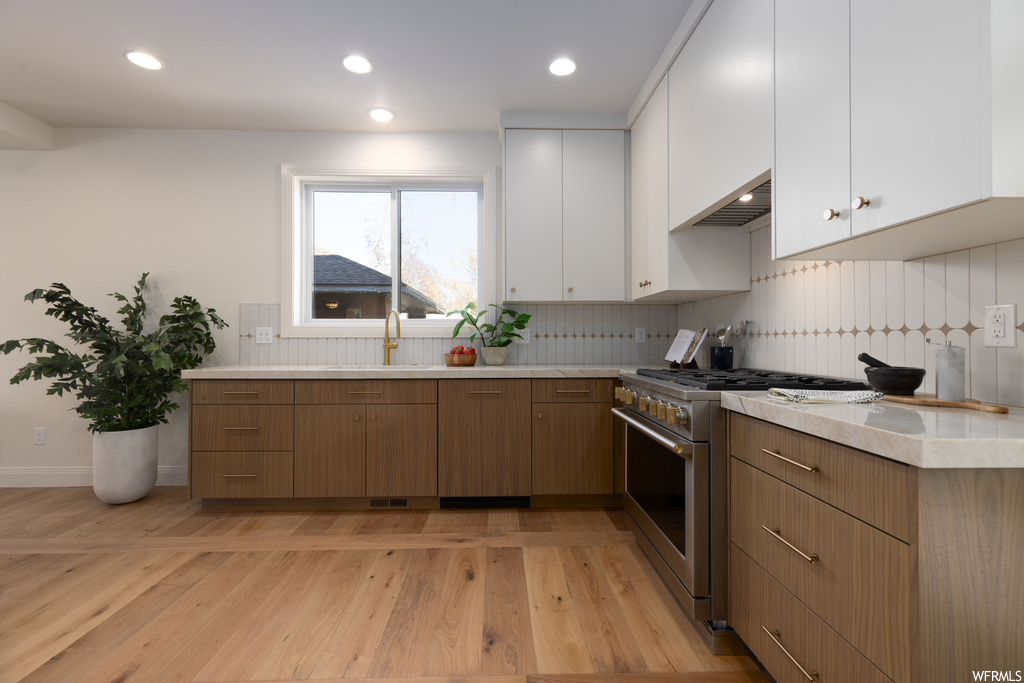Kitchen with tasteful backsplash, light wood-type flooring, stainless steel range, and white cabinetry