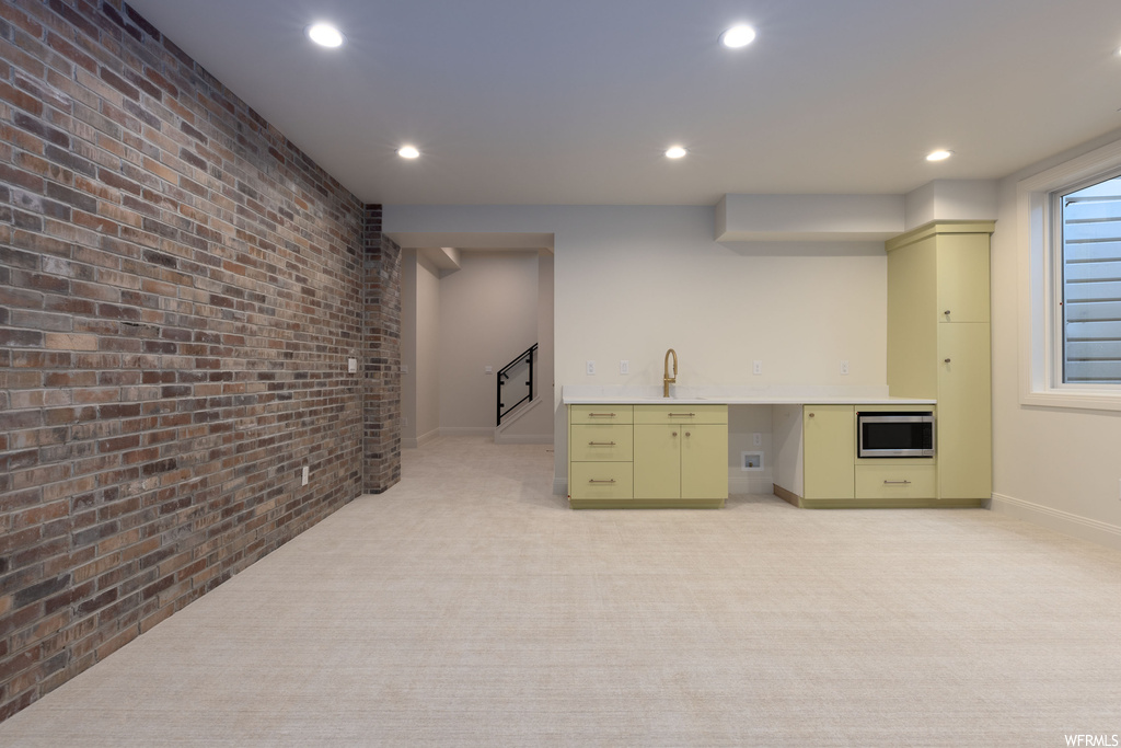 Interior space featuring light carpet, sink, brick wall, stainless steel microwave, and oven
