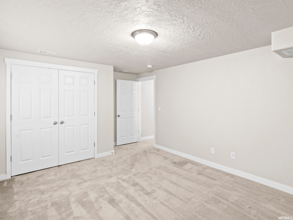 Unfurnished bedroom featuring a closet, light colored carpet, and a textured ceiling