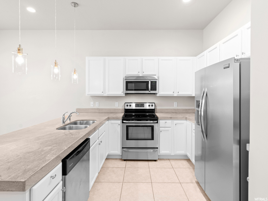 Kitchen featuring sink, white cabinets, appliances with stainless steel finishes, and pendant lighting