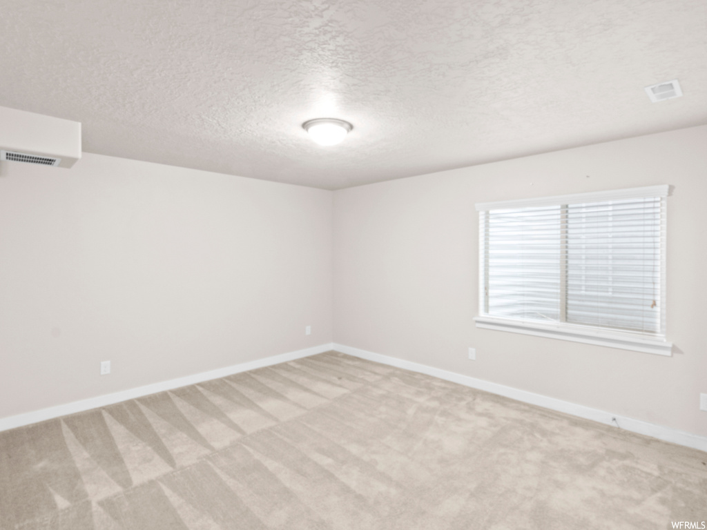 Unfurnished room featuring a textured ceiling, light carpet, and an AC wall unit