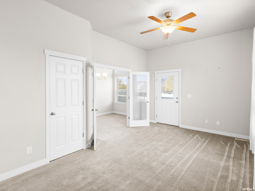 Unfurnished bedroom with ceiling fan with notable chandelier and light colored carpet