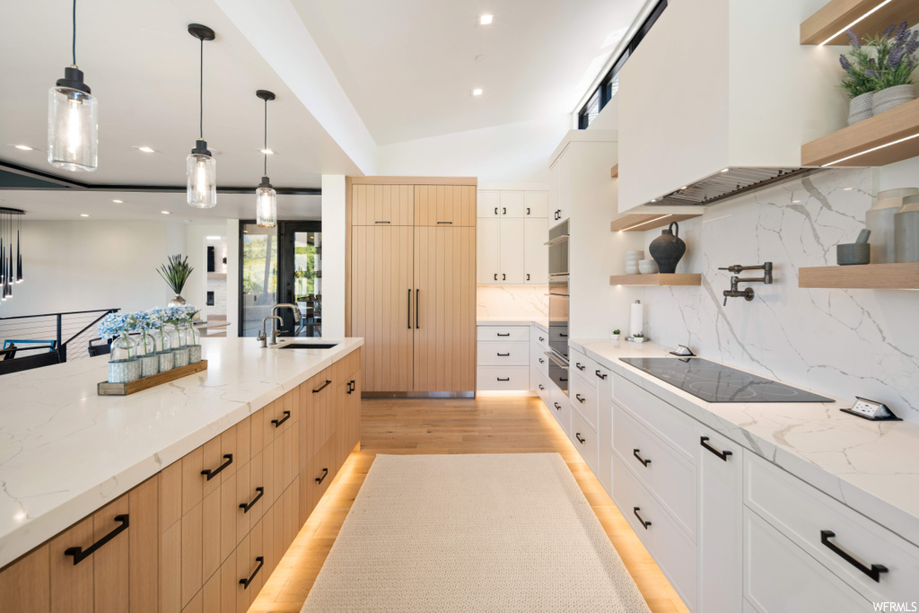 Kitchen featuring hanging light fixtures, tasteful backsplash, white cabinetry, and light hardwood / wood-style flooring