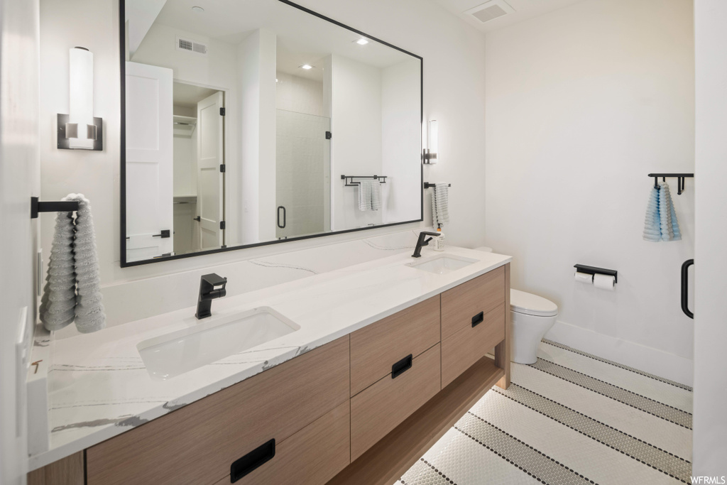 Bathroom featuring tile flooring, a shower with door, toilet, dual sinks, and oversized vanity
