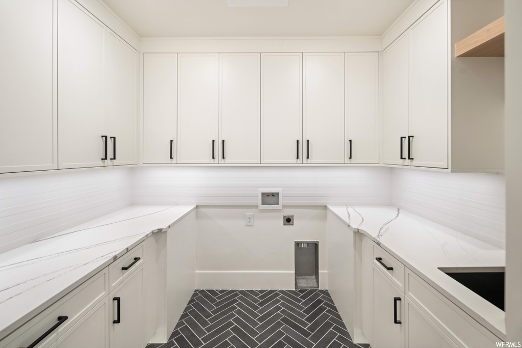 Laundry room featuring dark tile flooring, hookup for an electric dryer, and cabinets
