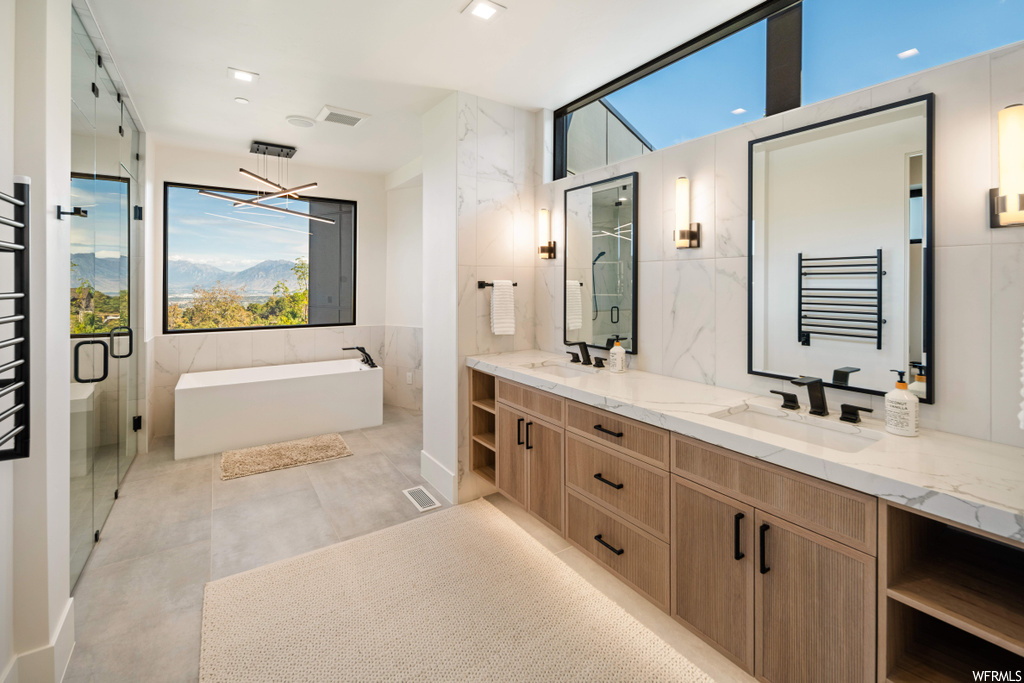 Bathroom with large vanity, tile flooring, double sink, tile walls, and separate shower and tub