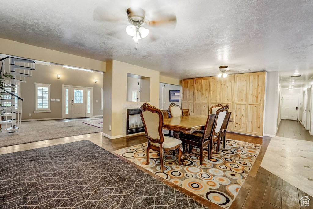 Carpeted dining room featuring a tiled fireplace, a textured ceiling, and ceiling fan