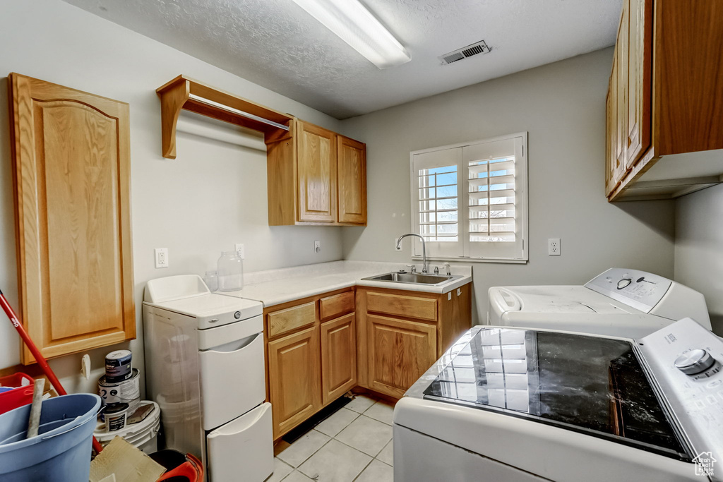 Laundry room with cabinets, washing machine and dryer, light tile floors, sink, and a textured ceiling