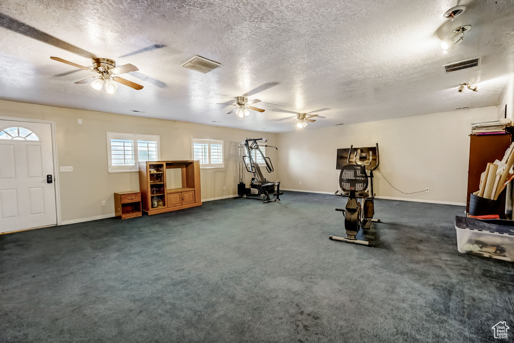 Exercise area featuring dark carpet, a textured ceiling, and ceiling fan