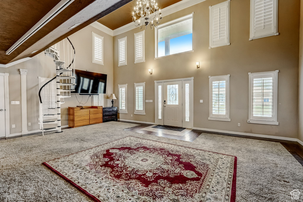 Foyer with crown molding, dark carpet, a high ceiling, and a notable chandelier