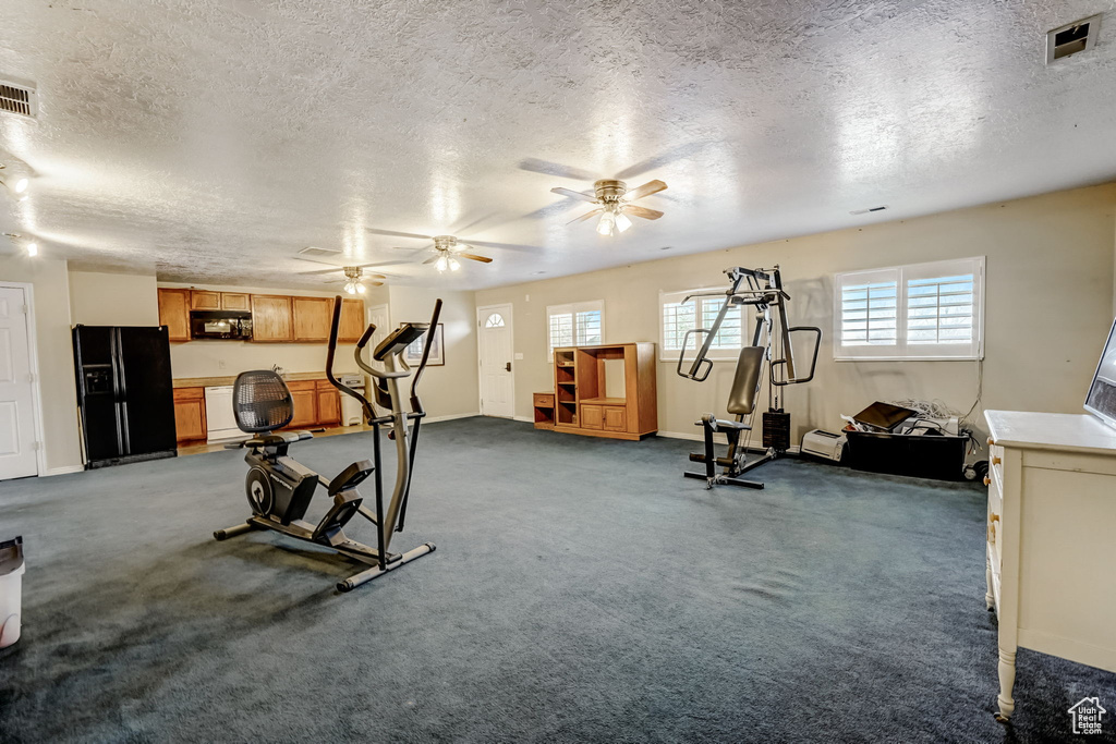Workout area featuring a textured ceiling, dark colored carpet, and ceiling fan