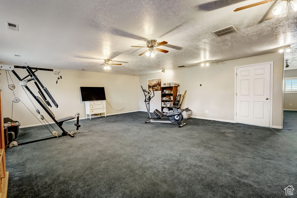 Exercise area with dark colored carpet, a textured ceiling, and ceiling fan