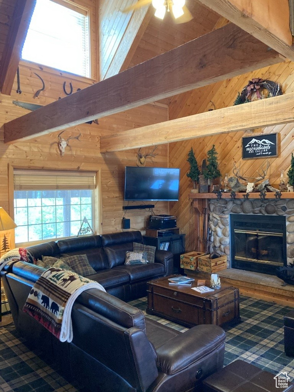 Living room with wood walls, ceiling fan, a stone fireplace, and beam ceiling