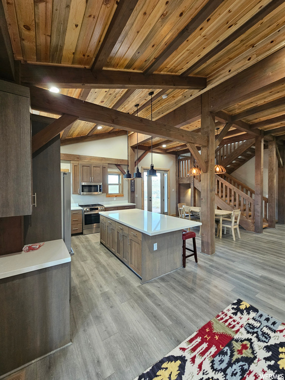 Kitchen with a center island, light hardwood / wood-style flooring, appliances with stainless steel finishes, hanging light fixtures, and lofted ceiling with beams