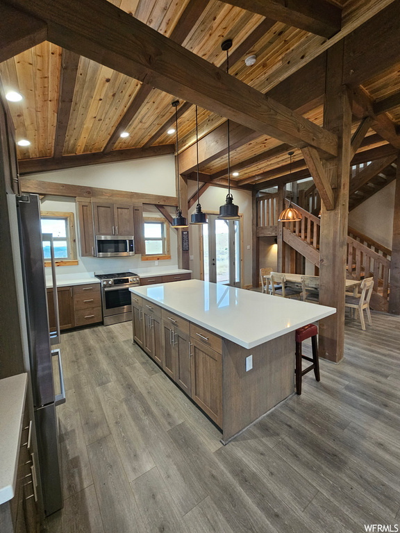 Kitchen with stainless steel appliances, a center island, decorative light fixtures, dark hardwood / wood-style flooring, and vaulted ceiling with beams