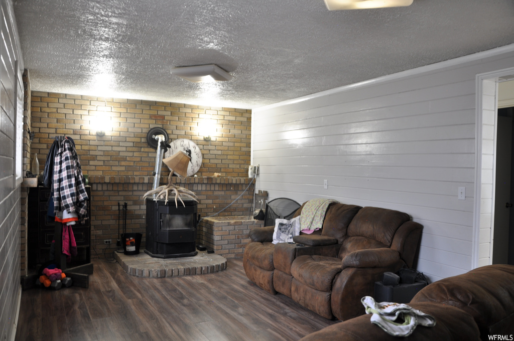 Living room with a textured ceiling, dark hardwood / wood-style flooring, a wood stove, and brick wall