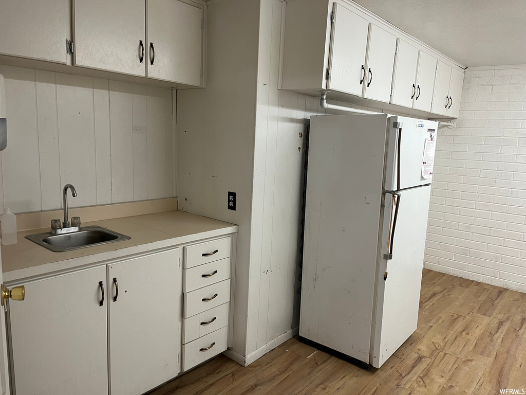 Kitchen with white refrigerator, brick wall, sink, light wood-type flooring, and white cabinets