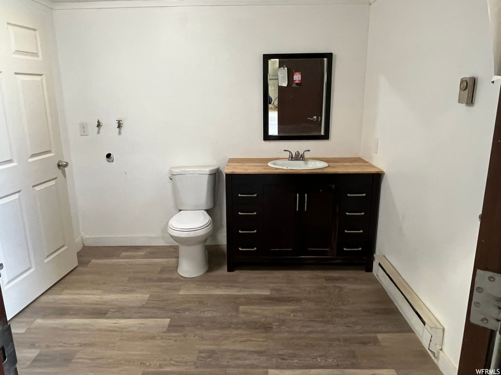 Bathroom featuring wood-type flooring, toilet, baseboard heating, and vanity with extensive cabinet space