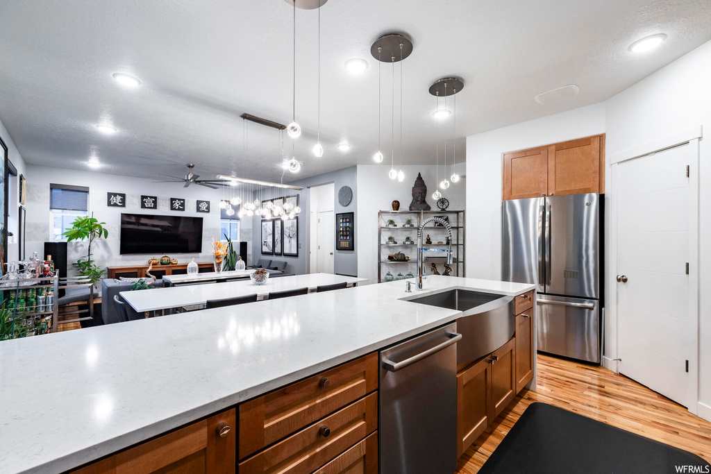 Kitchen featuring decorative light fixtures, sink, light hardwood / wood-style flooring, ceiling fan, and stainless steel appliances