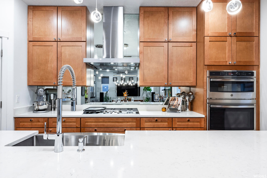 Kitchen with ventilation hood, sink, hanging light fixtures, and appliances with stainless steel finishes