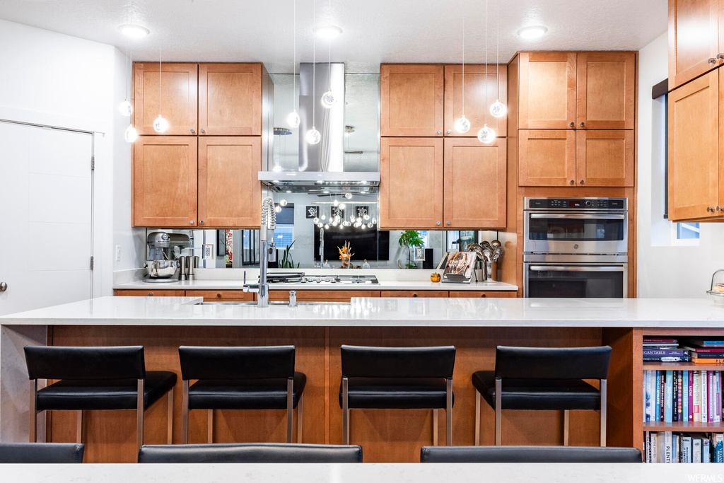 Kitchen with stainless steel double oven, wall chimney exhaust hood, and a kitchen island