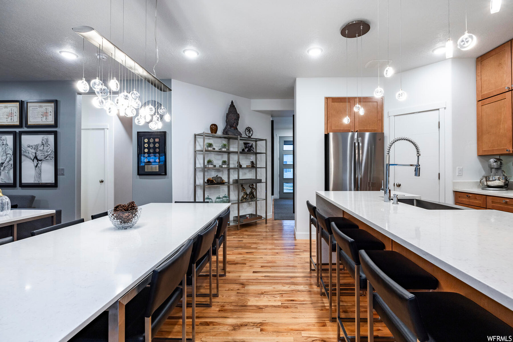 Kitchen with sink, stainless steel fridge, light wood-type flooring, pendant lighting, and a notable chandelier