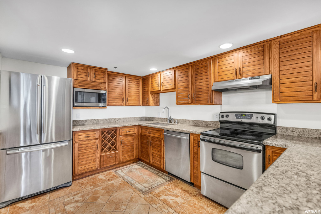Kitchen featuring stainless steel appliances, light stone countertops, light tile floors, and sink
