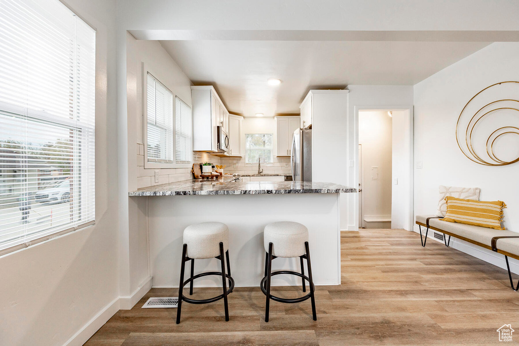 Kitchen featuring tasteful backsplash, light hardwood / wood-style floors, stainless steel appliances, and white cabinets