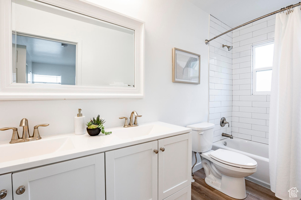 Full bathroom with hardwood / wood-style flooring, shower / bath combination with curtain, a healthy amount of sunlight, and vanity with extensive cabinet space