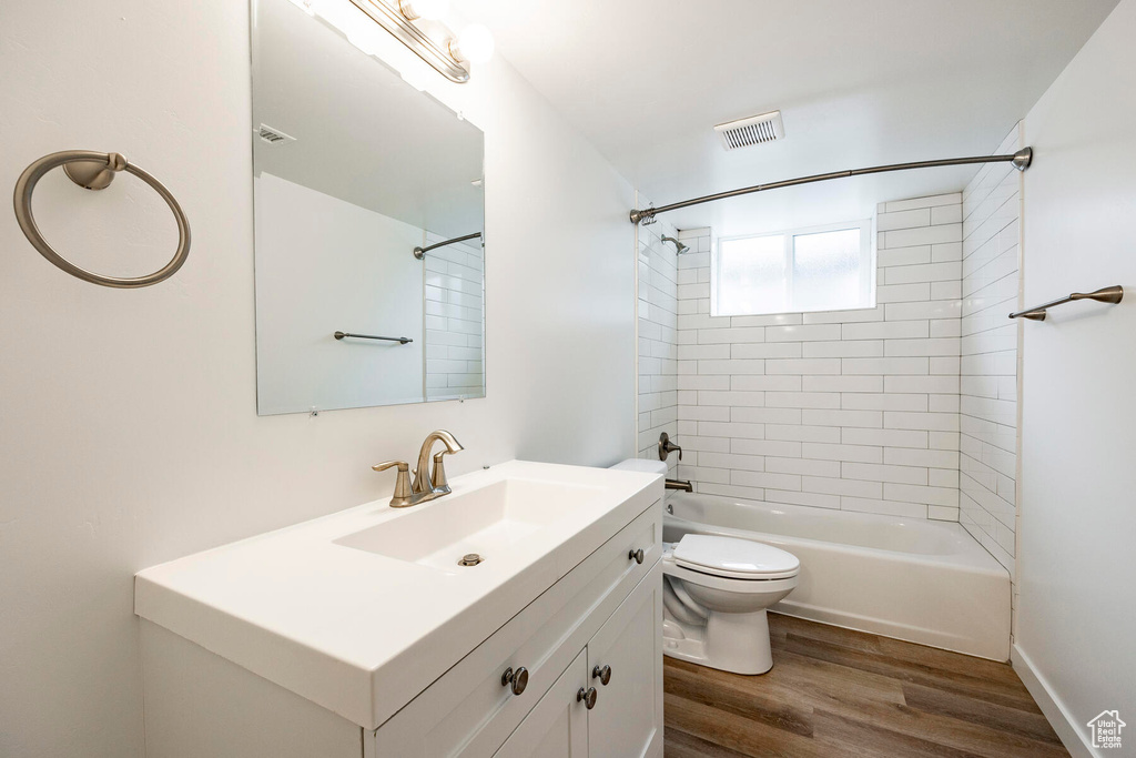 Full bathroom with vanity, toilet, tiled shower / bath combo, and hardwood / wood-style flooring