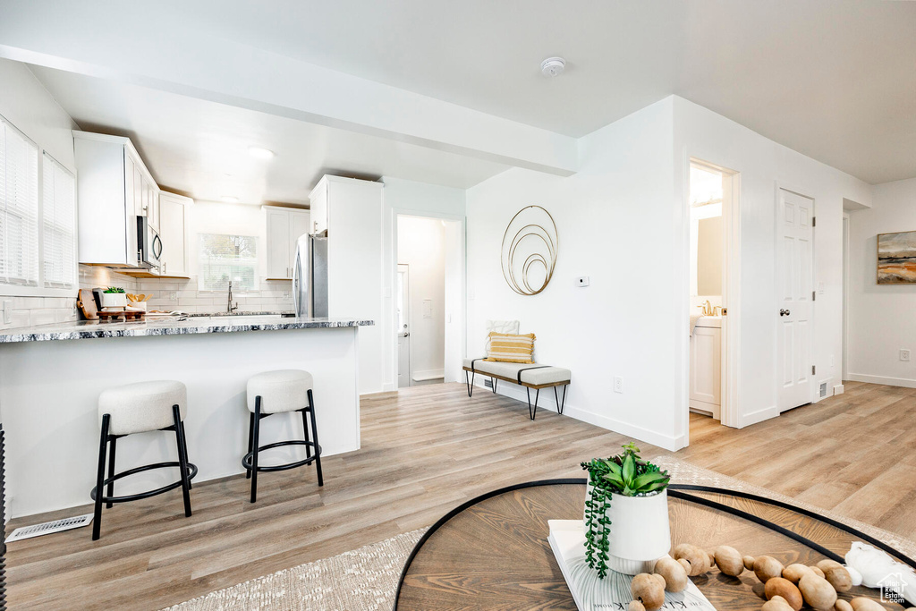 Kitchen with light hardwood / wood-style flooring, backsplash, white cabinets, a breakfast bar area, and light stone countertops