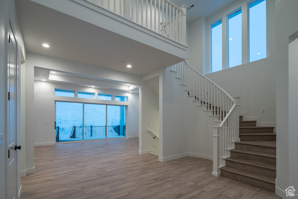 Stairs with plenty of natural light, light hardwood / wood-style flooring, and a high ceiling