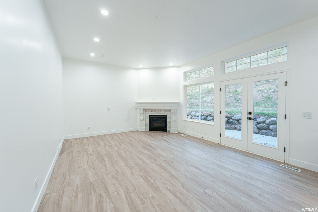 Unfurnished living room featuring french doors, a fireplace, and light hardwood / wood-style flooring