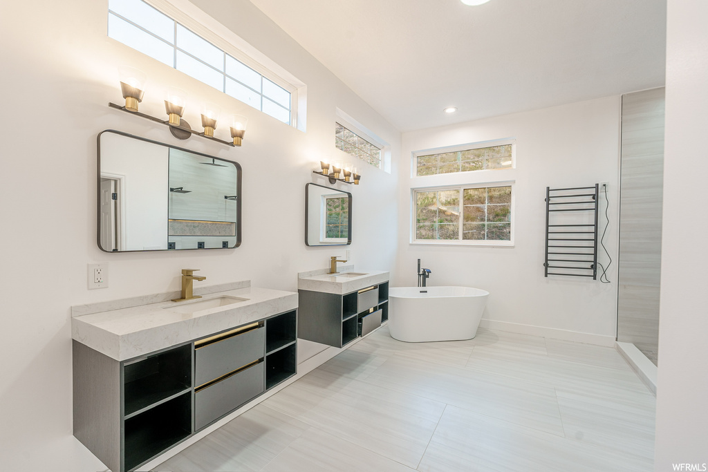 Bathroom with tile flooring, a tub, a healthy amount of sunlight, and double sink vanity