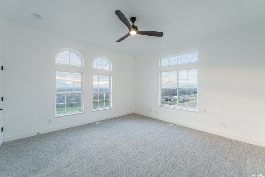 Carpeted empty room featuring plenty of natural light and ceiling fan