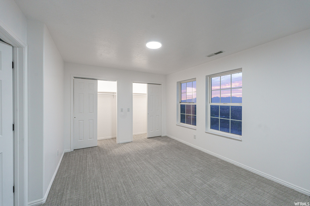 Unfurnished bedroom with two closets and light colored carpet