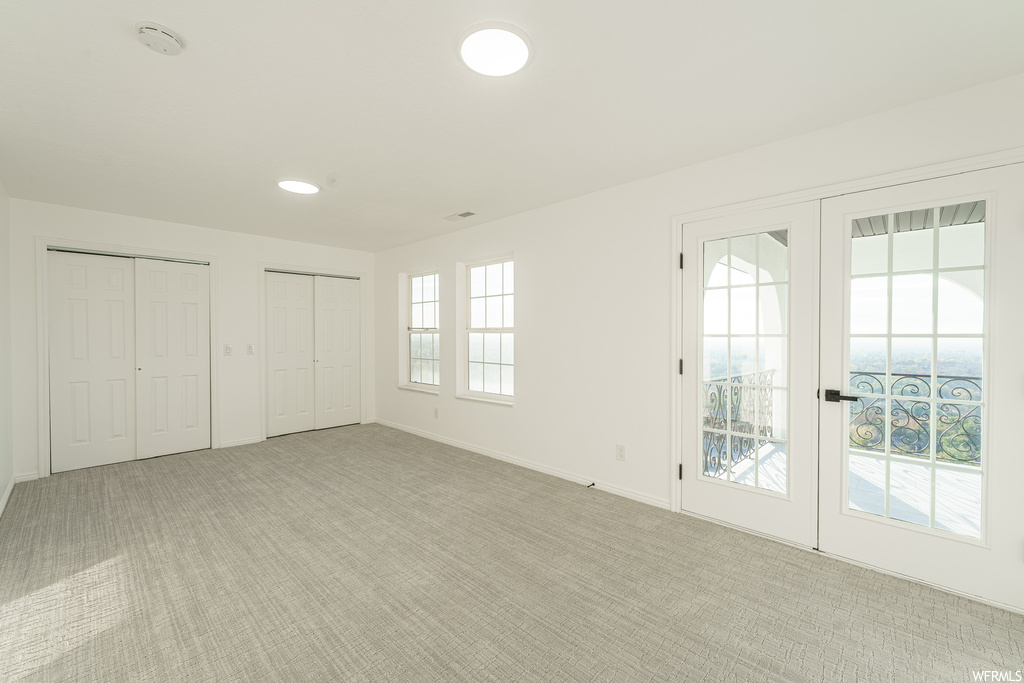 Unfurnished bedroom with multiple closets, light carpet, and french doors